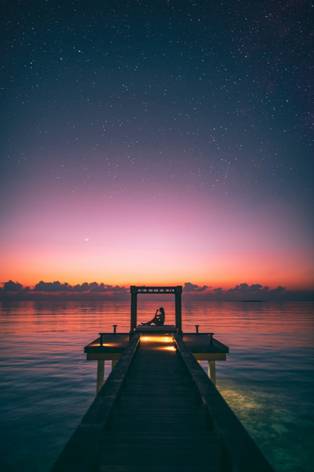 a girl sitting on a boardwalk during sunset on the sea