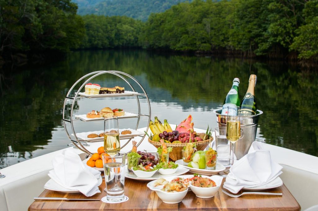 A table laid out on a boat with several wine varieties, fruits, desserts, and fish.