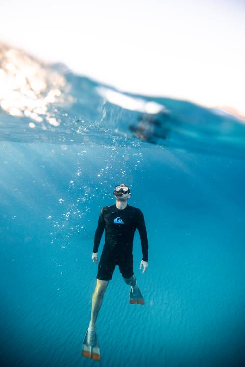 A man in a black swimsuit and snorkeling gear in the sea.